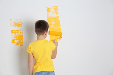 Photo of Little child painting wall with roller brush indoors