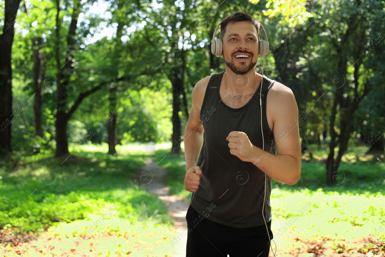 Photo of Handsome man with headphones running in park, space for text. Morning exercise