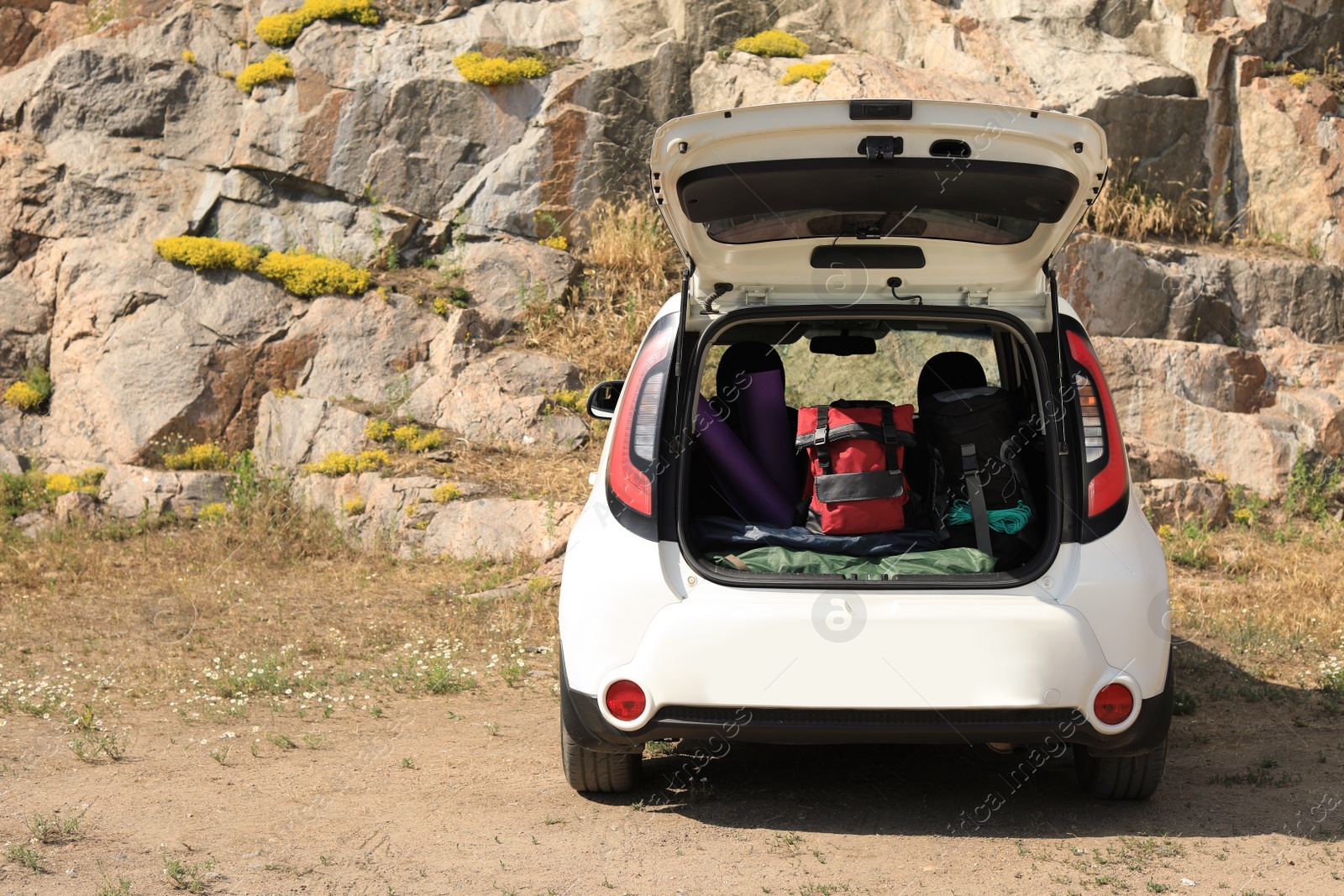 Photo of Car with camping equipment in trunk near rocky cliff. Space for text