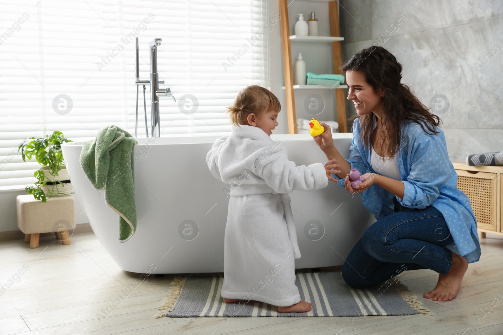 Photo of Mother playing with her daughter near tub in bathroom
