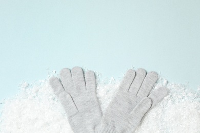 Photo of Stylish woolen gloves and artificial snow on light blue background, flat lay. Space for text