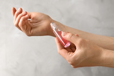 Photo of Woman applying rose essential oil on wrist against color background, closeup