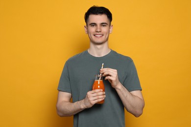 Photo of Handsome young man with glassjuice on orange background