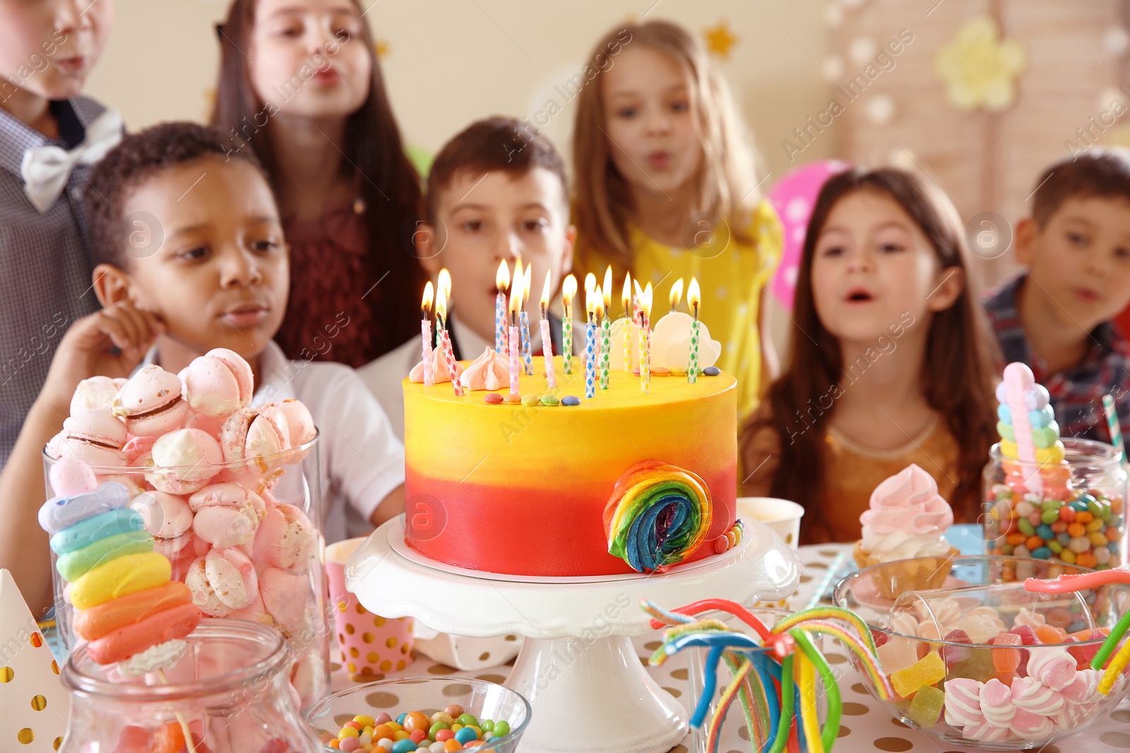 Photo of Cute children blowing out candles on birthday cake at table indoors