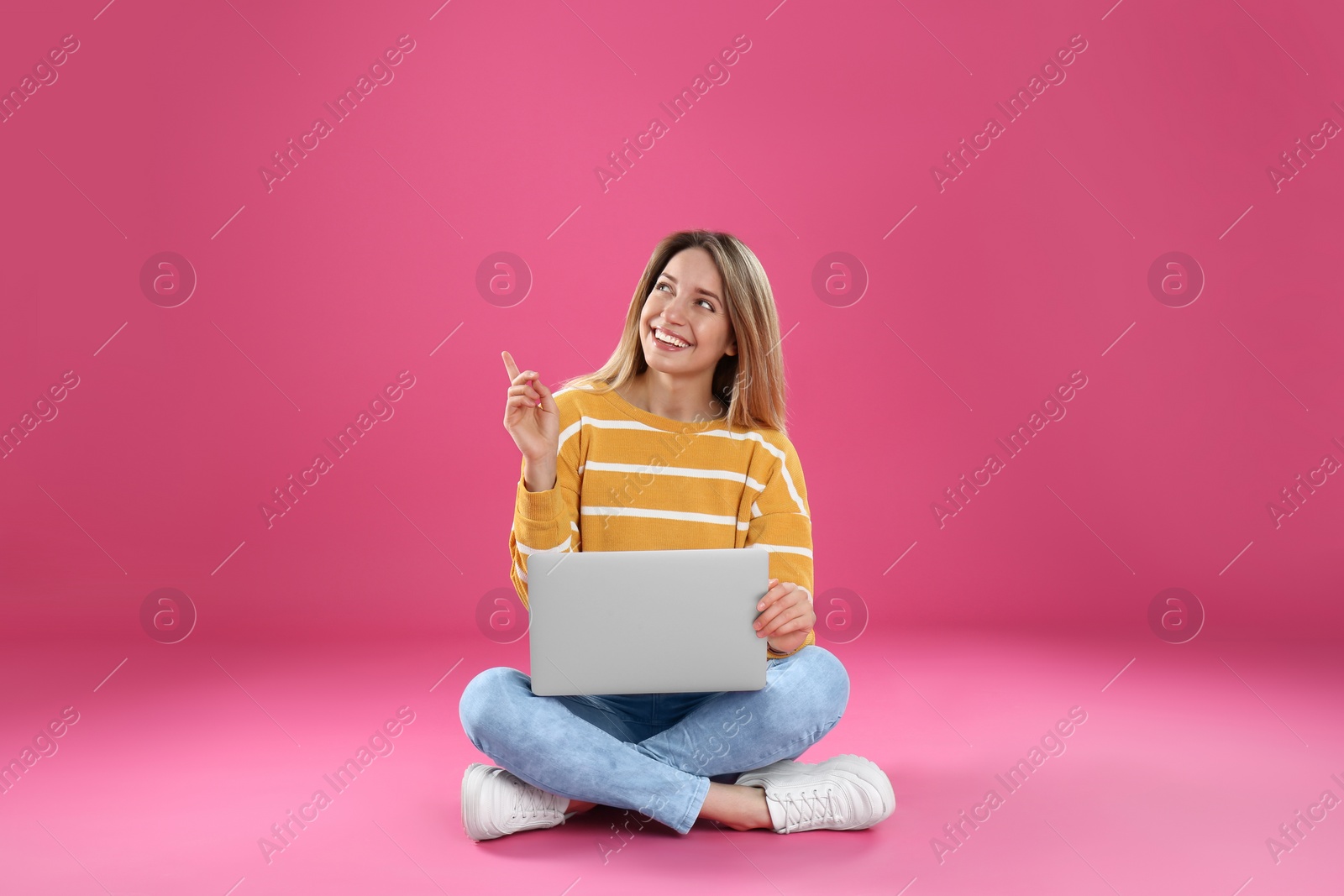 Photo of Young woman in casual outfit with laptop sitting on color background