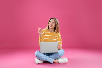 Photo of Young woman in casual outfit with laptop sitting on color background