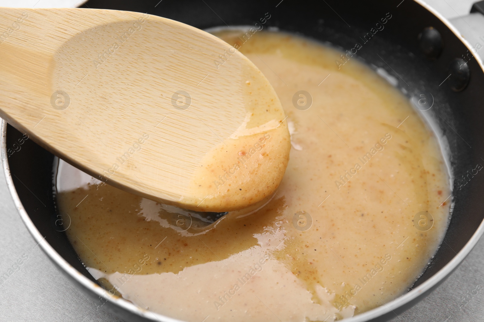 Photo of Stirring delicious turkey gravy in frying pan on table, closeup