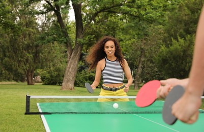 Young African-American woman playing ping pong with friend outdoors
