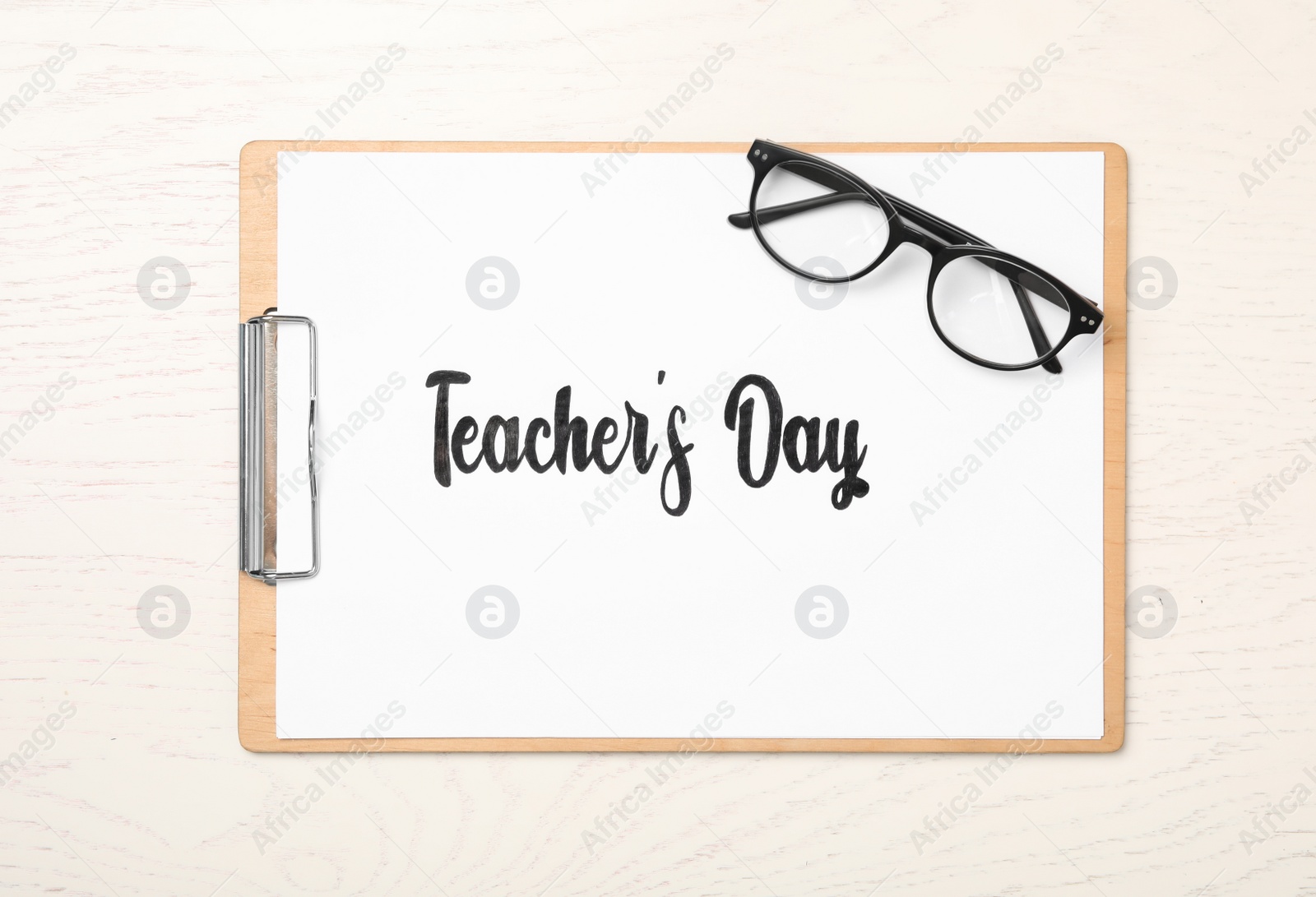 Photo of Clipboard with words TEACHER'S DAY and glasses on white wooden background, top view