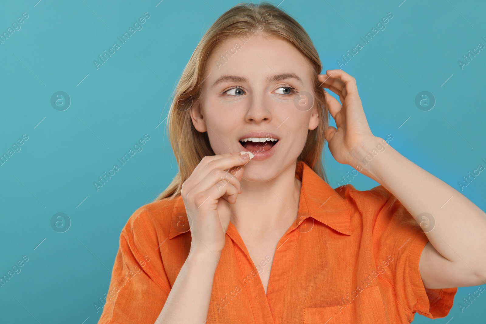 Photo of Happy young woman putting bubble gum into mouth on light blue background
