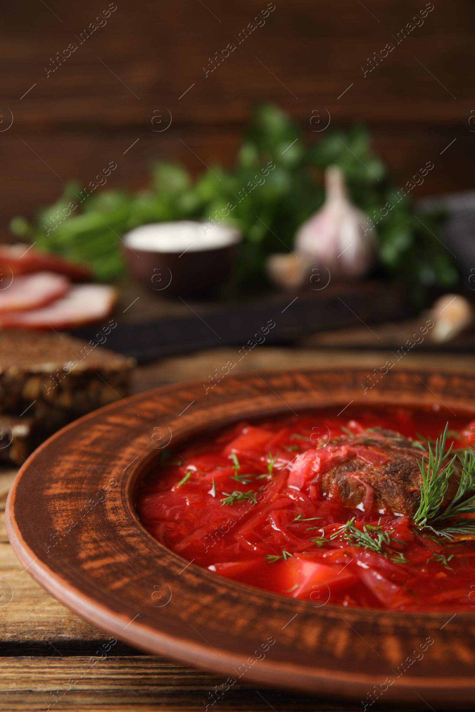 Photo of Stylish brown clay plate with Ukrainian borsch served on wooden table, closeup