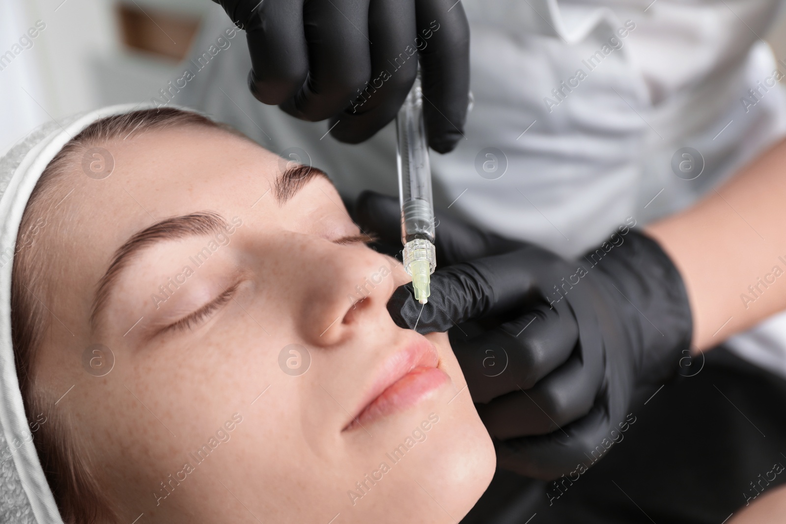 Photo of Cosmetologist giving lips injection to patient indoors, closeup. Cosmetic surgery