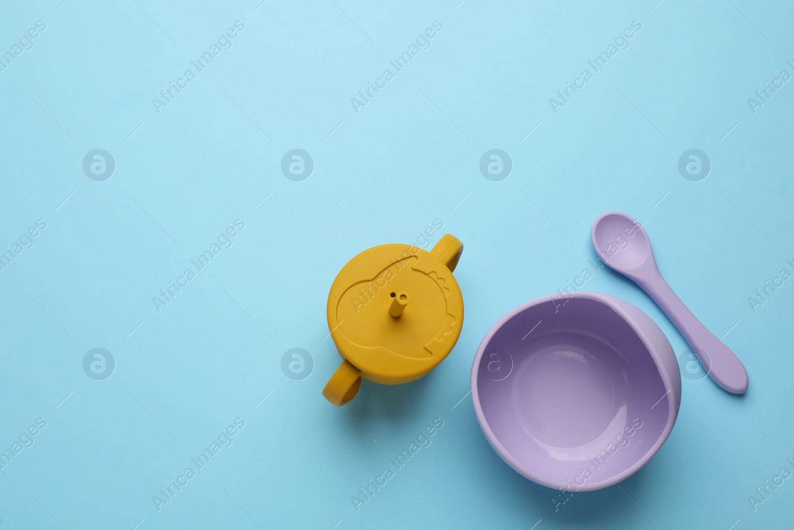 Photo of Set of plastic dishware on light blue background, flat lay with space for text. Serving baby food