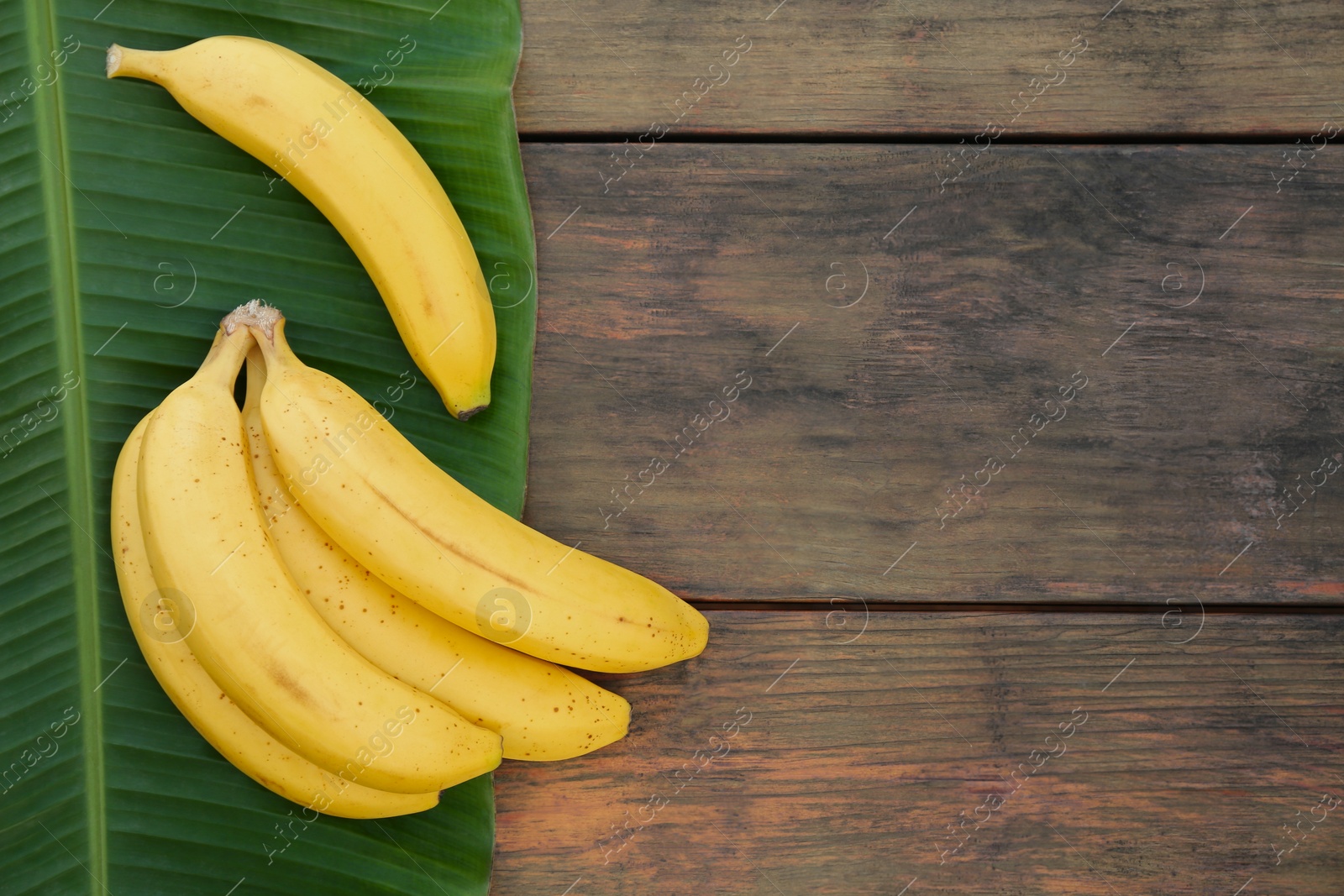 Photo of Delicious bananas and green leaf on wooden table, top view. Space for text