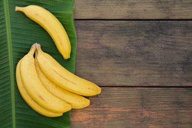 Photo of Delicious bananas and green leaf on wooden table, top view. Space for text