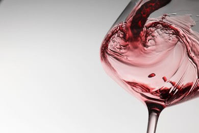 Pouring tasty red wine in glass on white background, closeup. Space for text