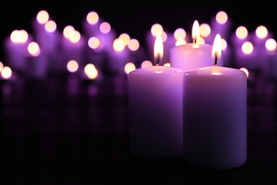 Image of Beautiful burning violet candles on black background. Funeral attributes