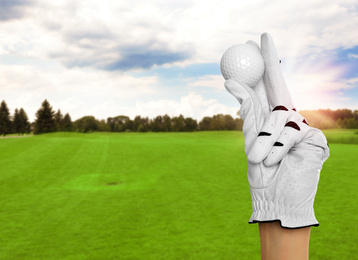 Player holding golf ball in park on sunny day, closeup. Space for design