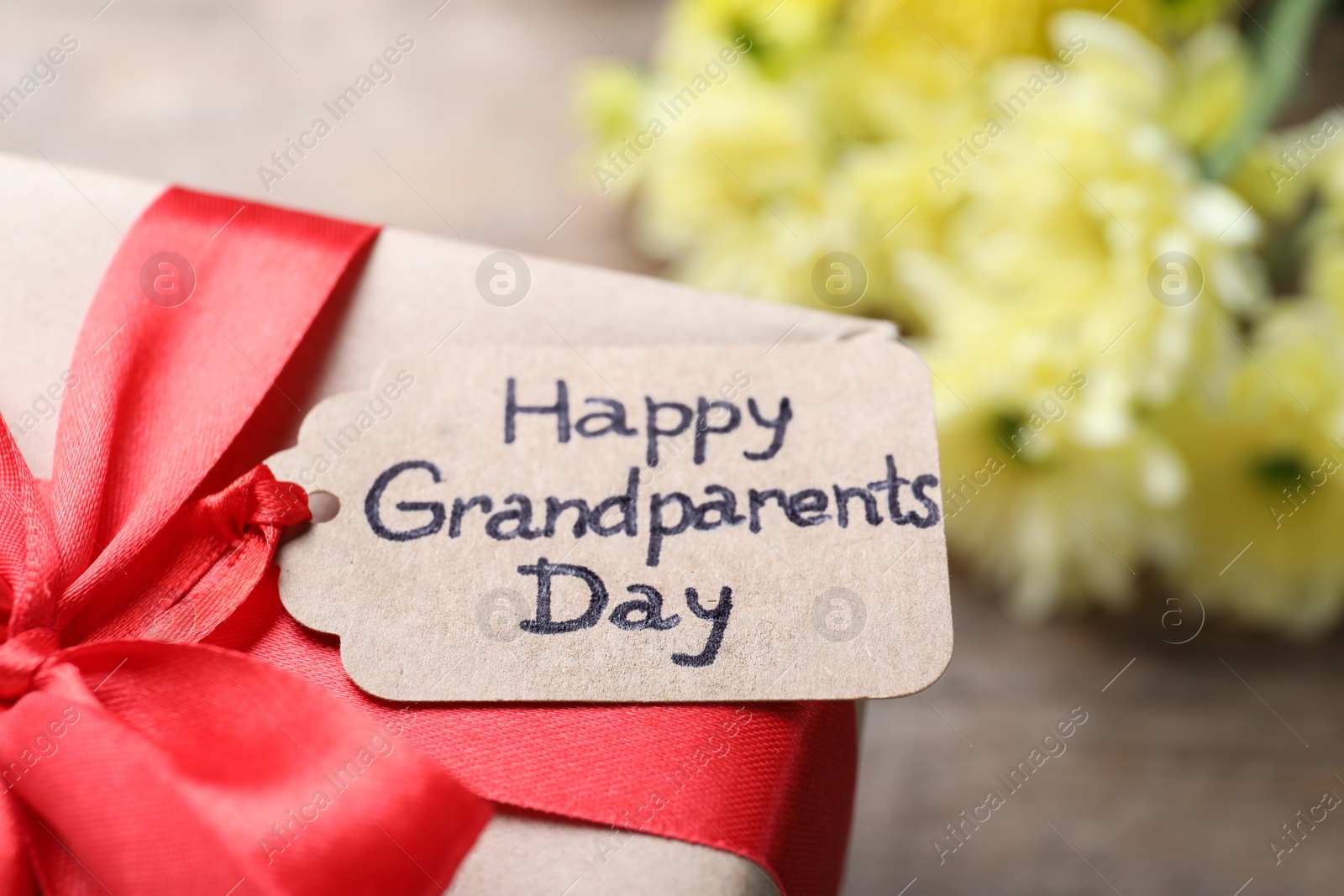 Photo of Beautiful gift box and tag with phrase Happy Grandparents Day on table, closeup