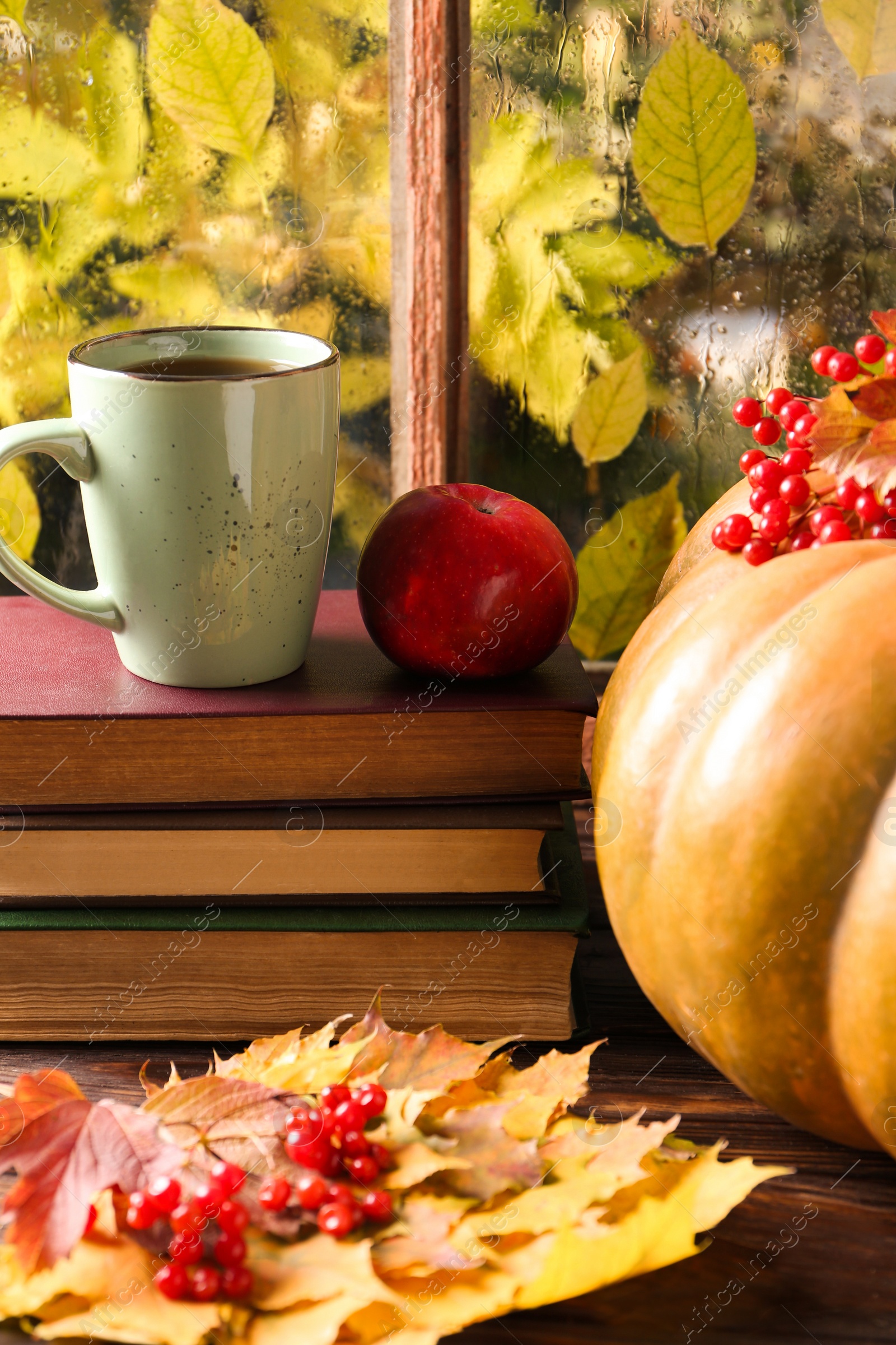 Photo of Stack of books, cup with aromatic tea, pumpkin and dry leaves on wooden windowsill indoors. Autumn atmosphere