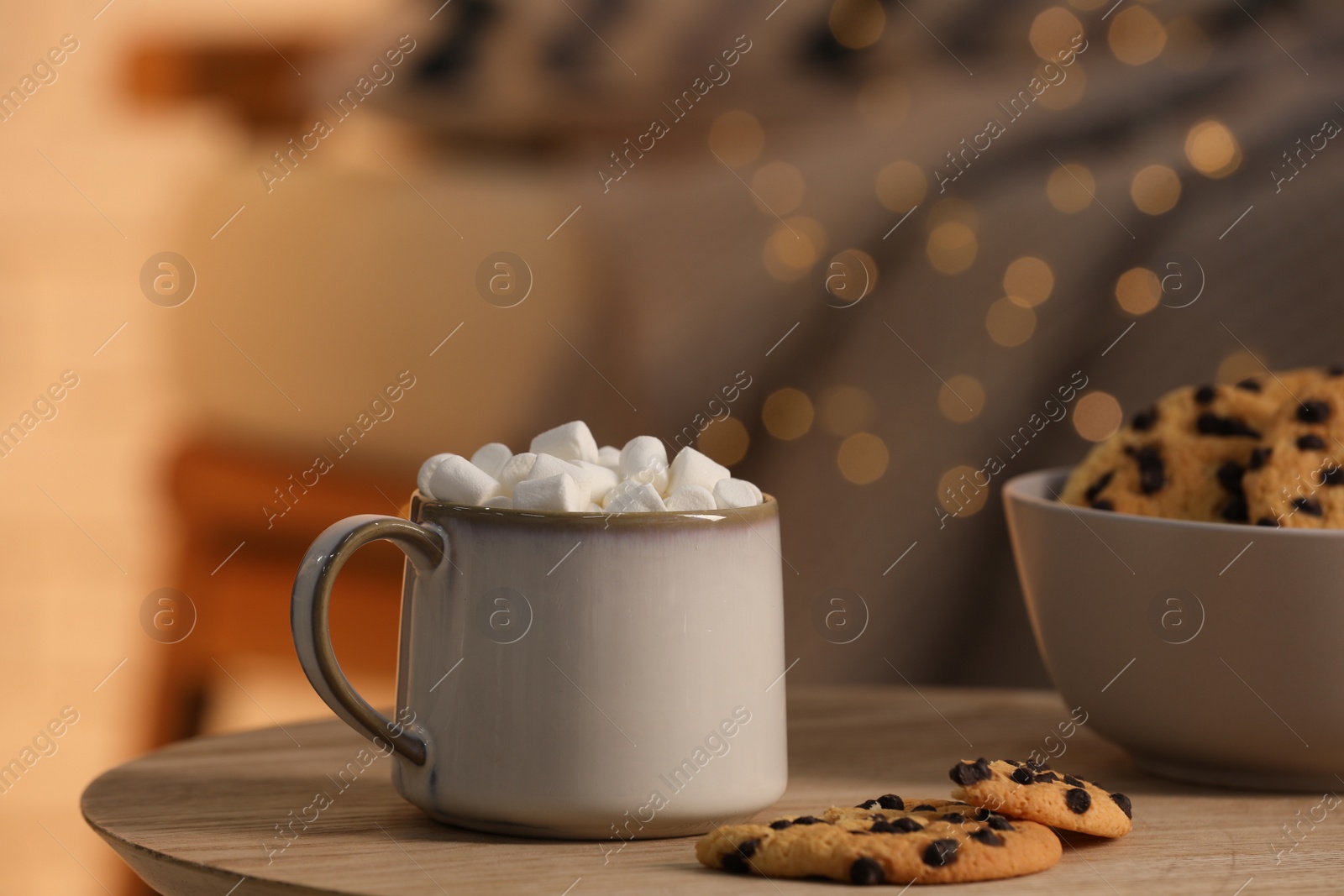 Photo of Mug of hot cocoa with marshmallows and cookies in bowl on wooden table indoors