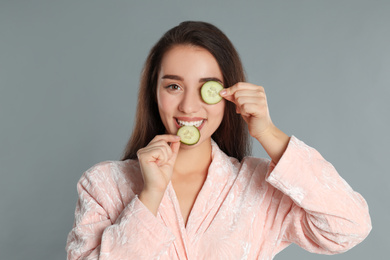 Photo of Young woman in bathrobe with cucumber slices on grey background