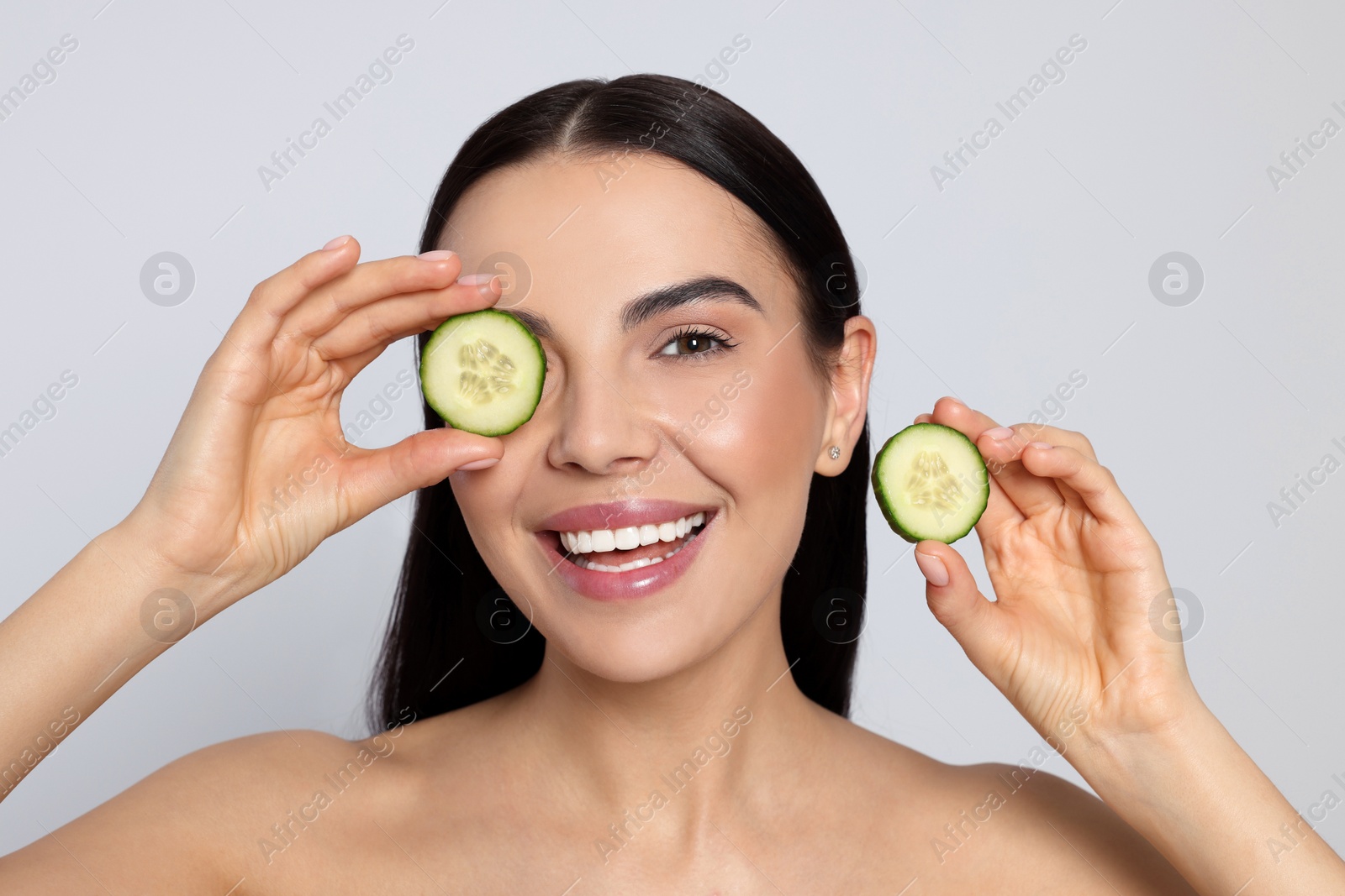 Photo of Woman holding pieces of cucumber on light grey background. Spa treatment