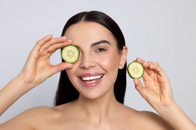 Woman holding pieces of cucumber on light grey background. Spa treatment