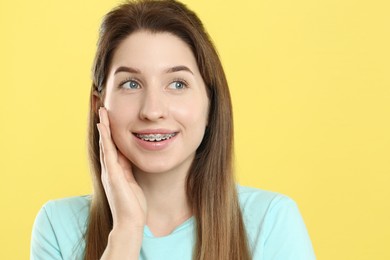 Portrait of smiling woman with dental braces on yellow background