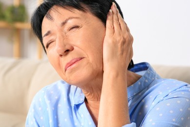 Photo of Senior woman suffering from ear pain at home, closeup
