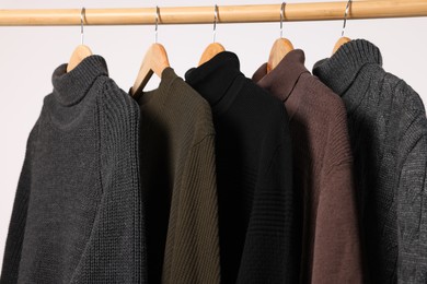 Rack with different casual sweaters on light background