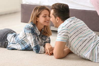 Photo of Lovely young couple lying on cozy carpet at home