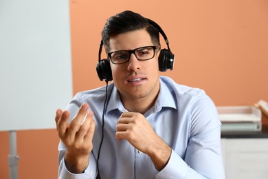 Photo of Man with headset holding online webinar indoors, view from webcam