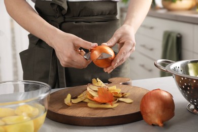 Photo of Woman peeling fresh onion with knife at table indoors, closeup