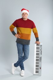 Man in Santa hat with synthesizer on light grey background. Christmas music
