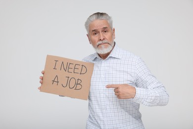 Photo of Unemployed senior man pointing at cardboard sign with phrase I Need A Job on white background