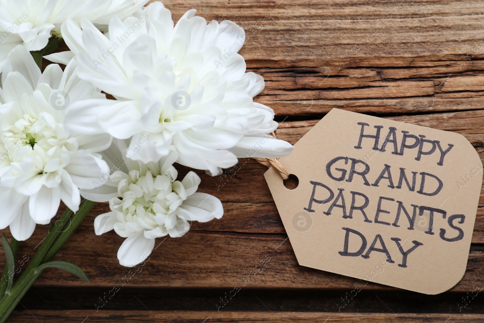Photo of Beautiful white flowers and tag with phrase Happy Grandparents Day on wooden background, flat lay