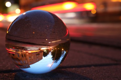 Photo of Beautiful city street, overturned reflection. Crystal ball on asphalt road at night, closeup. Space for text