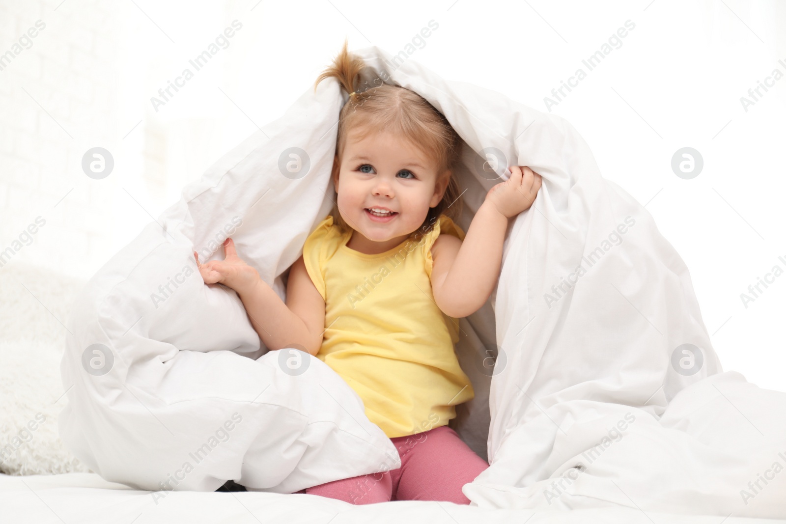 Photo of Cute little child playing under blanket in bed