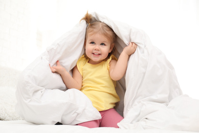 Photo of Cute little child playing under blanket in bed