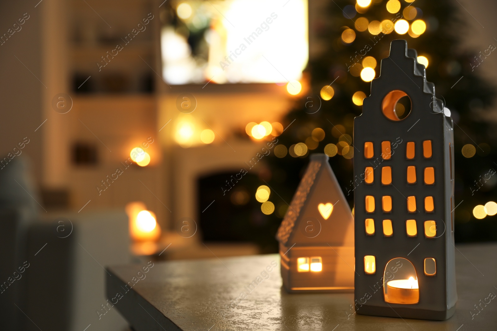 Photo of Beautiful house shaped candle holders on table indoors, space for text. Bokeh effect