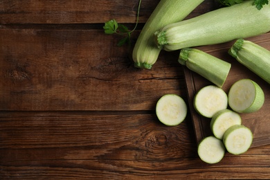 Photo of Cut and whole ripe zucchinis on wooden table, flat lay. Space for text