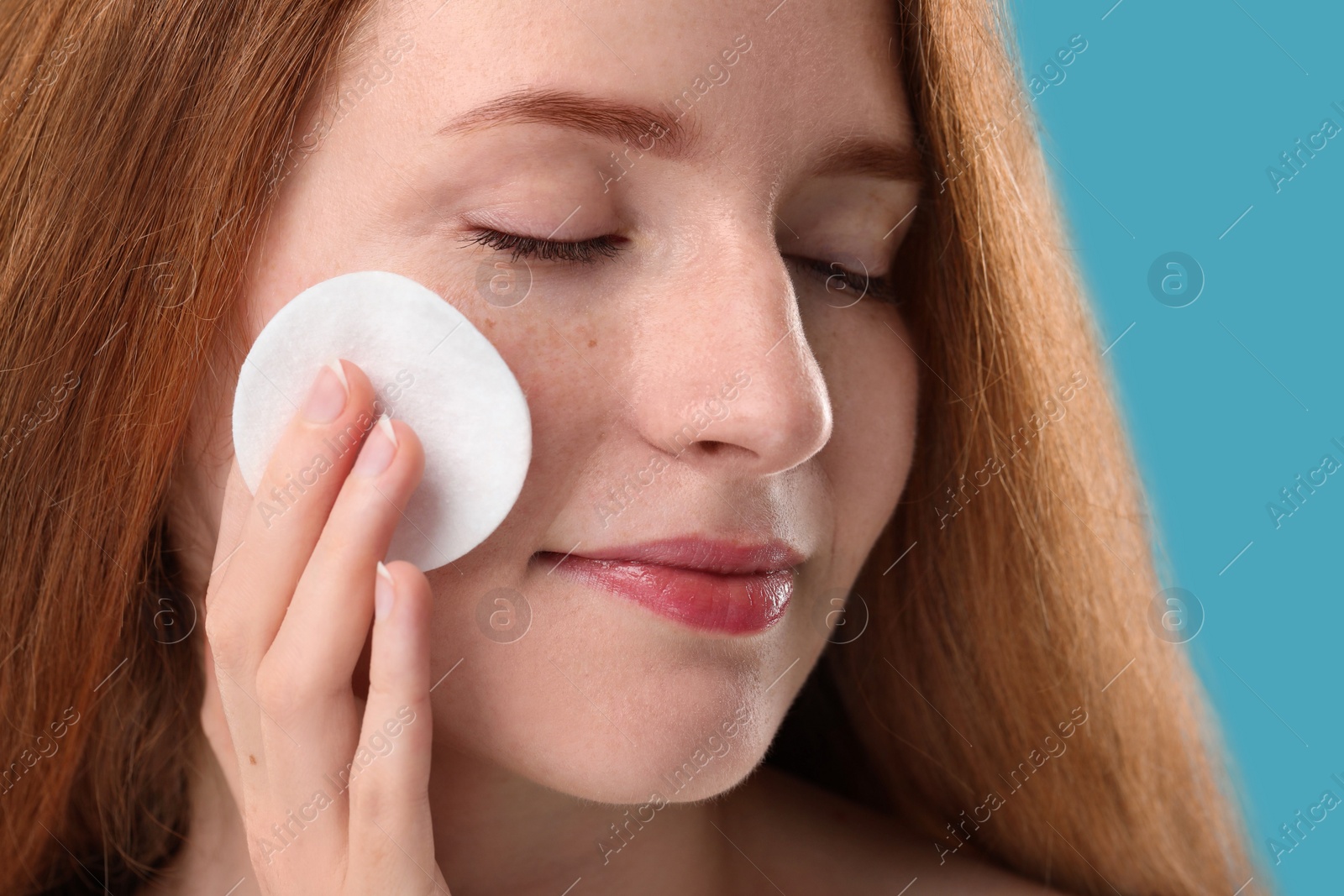 Photo of Beautiful woman with freckles wiping face on light blue background, closeup