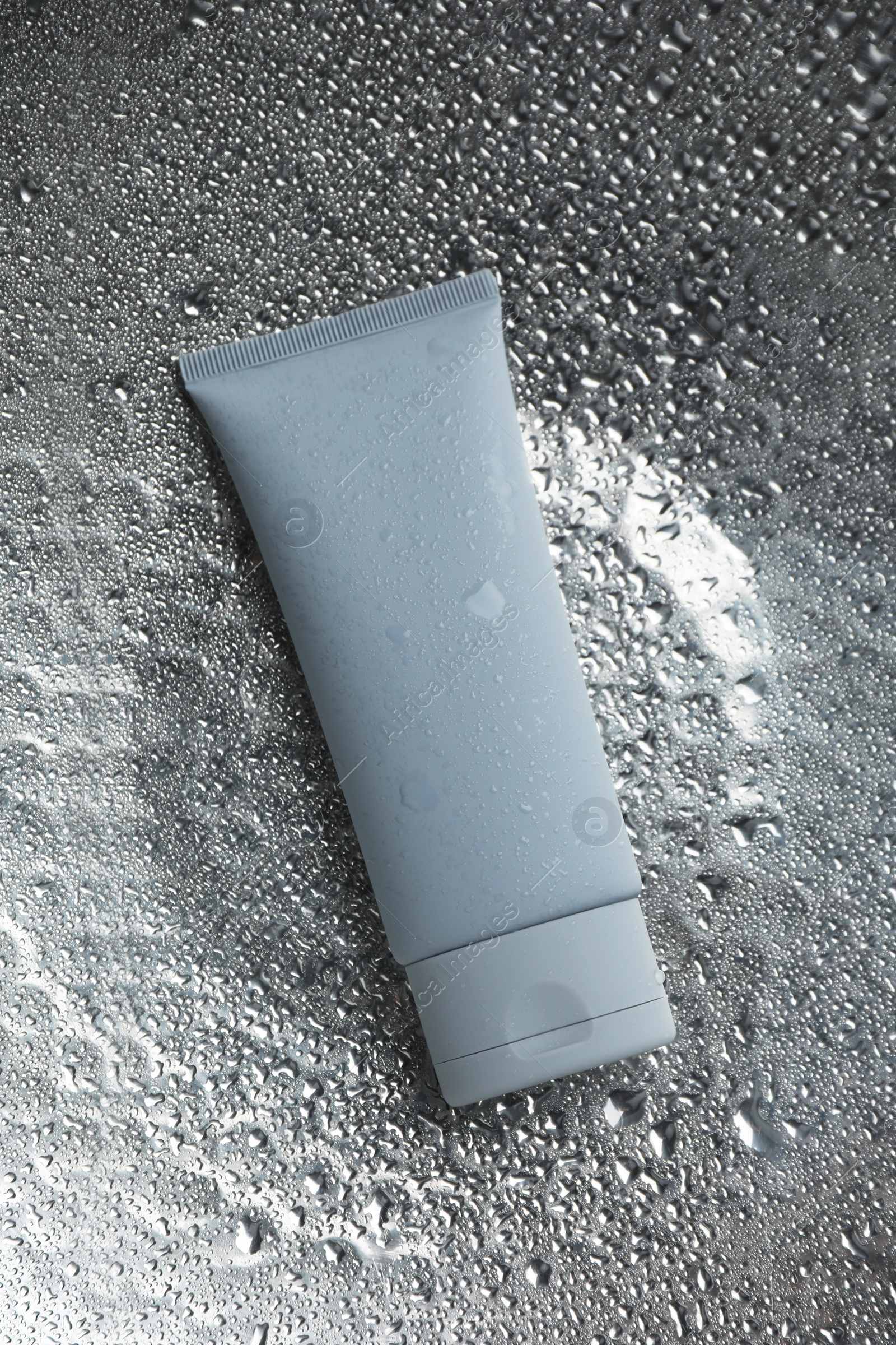 Photo of Moisturizing cream in tube on silver background with water drops, top view