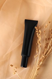Tube of skin foundation and decorative plants on beige tulle fabric, flat lay. Makeup product