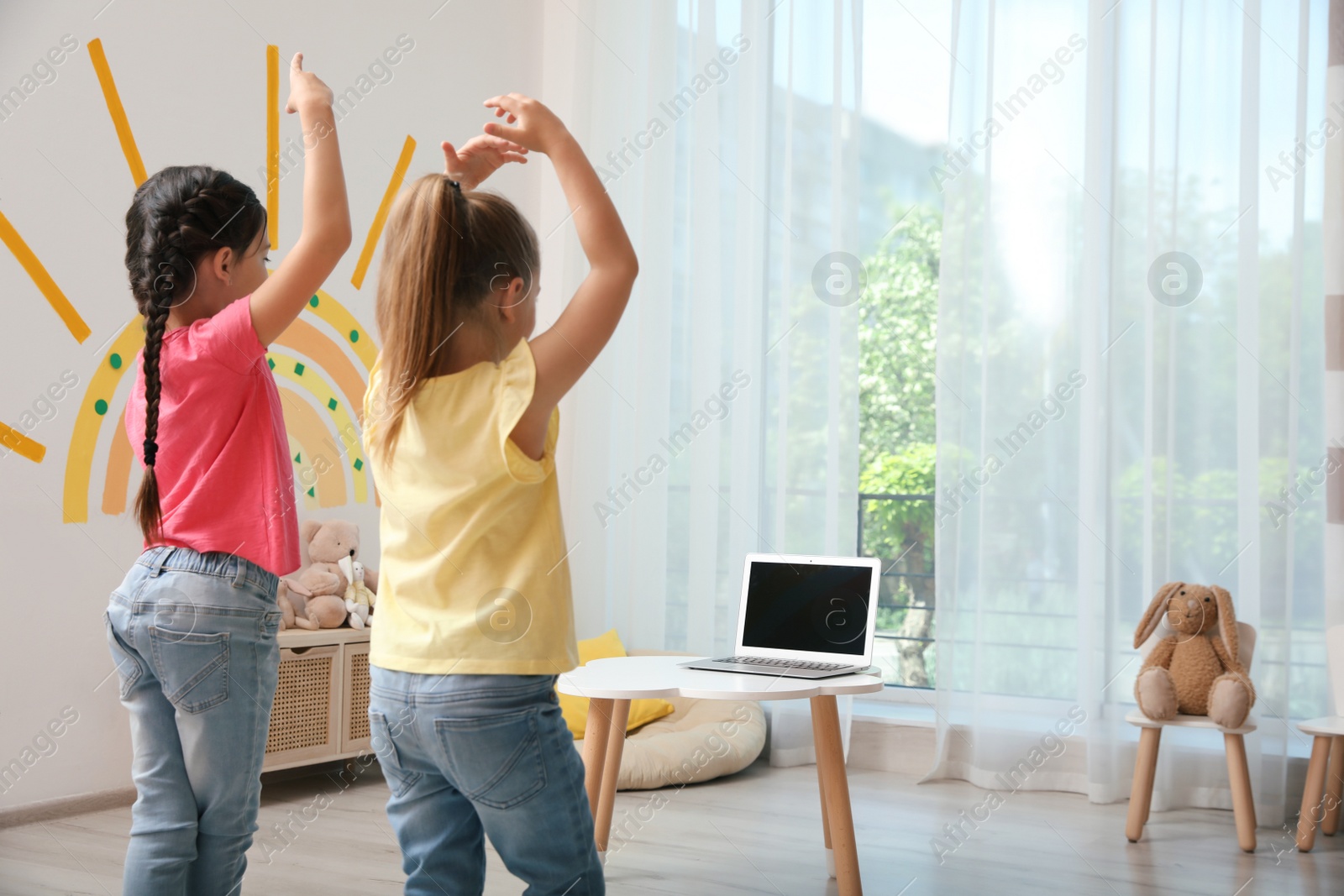 Photo of Cute little girls taking online dance class indoors, back view