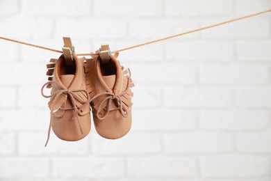 Cute baby shoes drying on washing line against white brick wall. Space for text