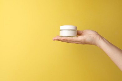Photo of Woman holding jar of face cream on yellow background, closeup. Space for text