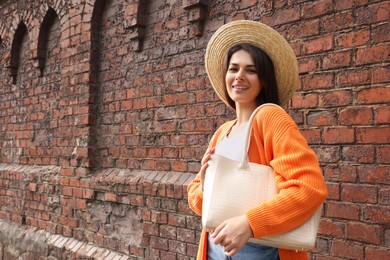 Photo of Young woman with stylish bag near red brick wall outdoors, space for text