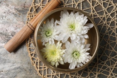 Photo of Tibetan singing bowl with water, beautiful chrysanthemum flowers and mallet on table, top view
